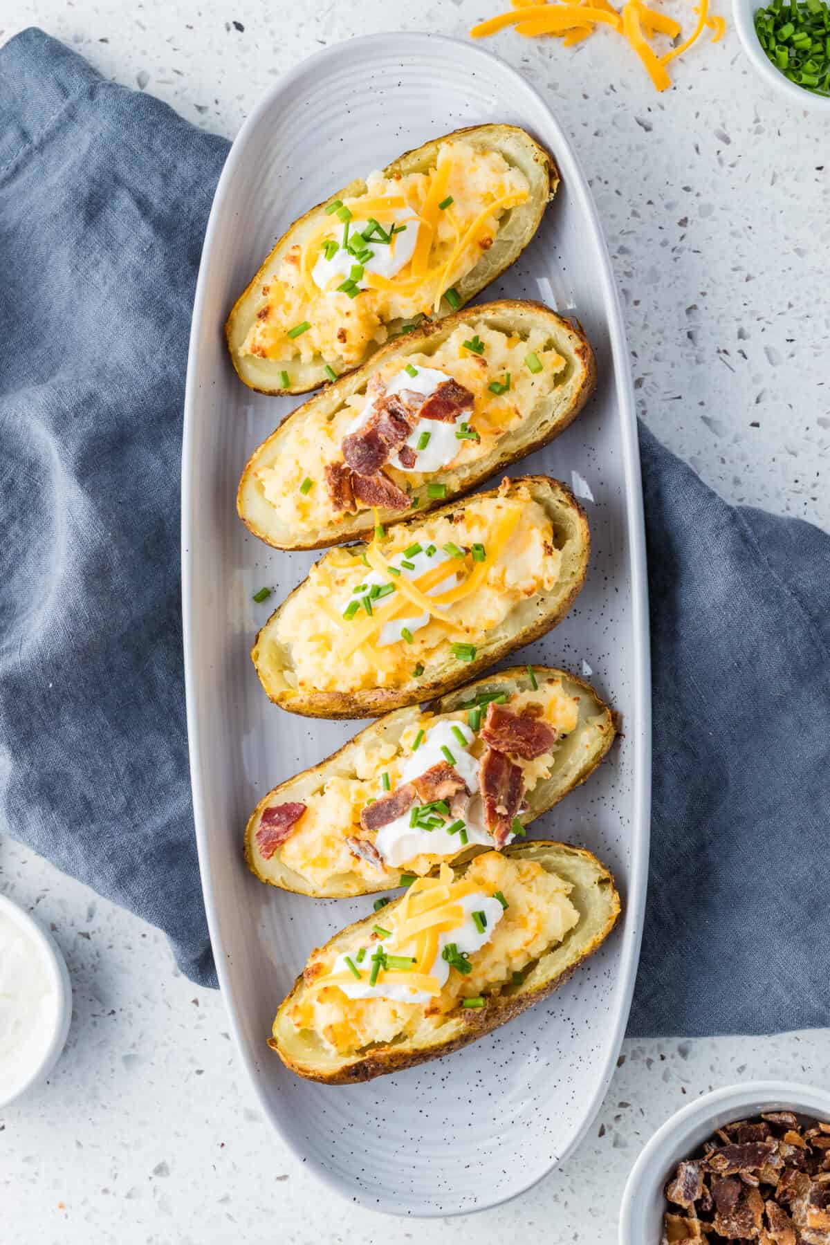 twice baked potatoes on cookie sheet with sour cream, cheese and bacon pieces