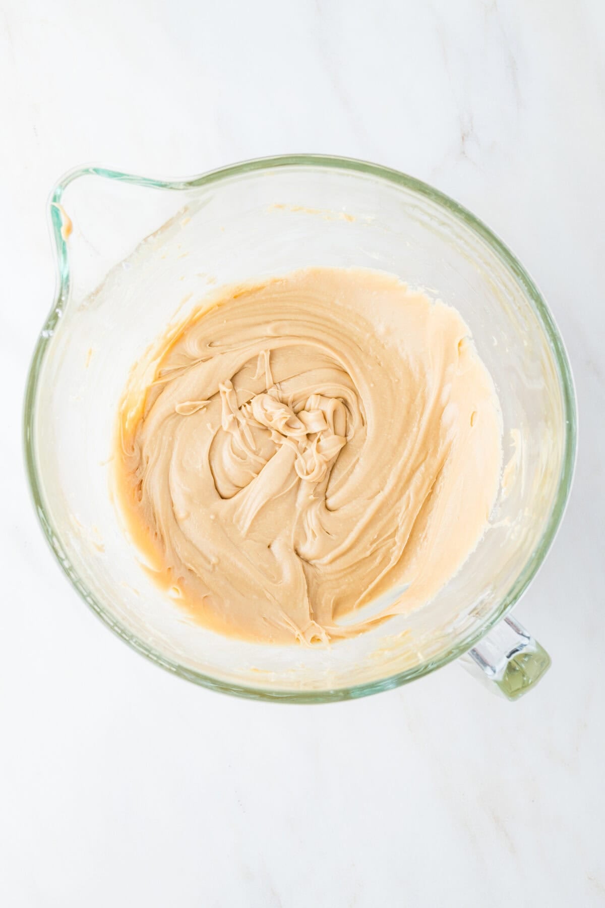 caramel icing in a mixing bowl with confectioners sugar added