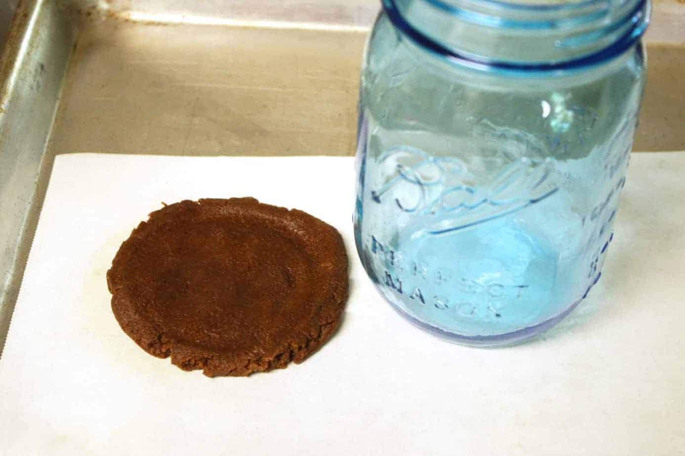 chocolate cookie dough flattened on parchment paper by a glass