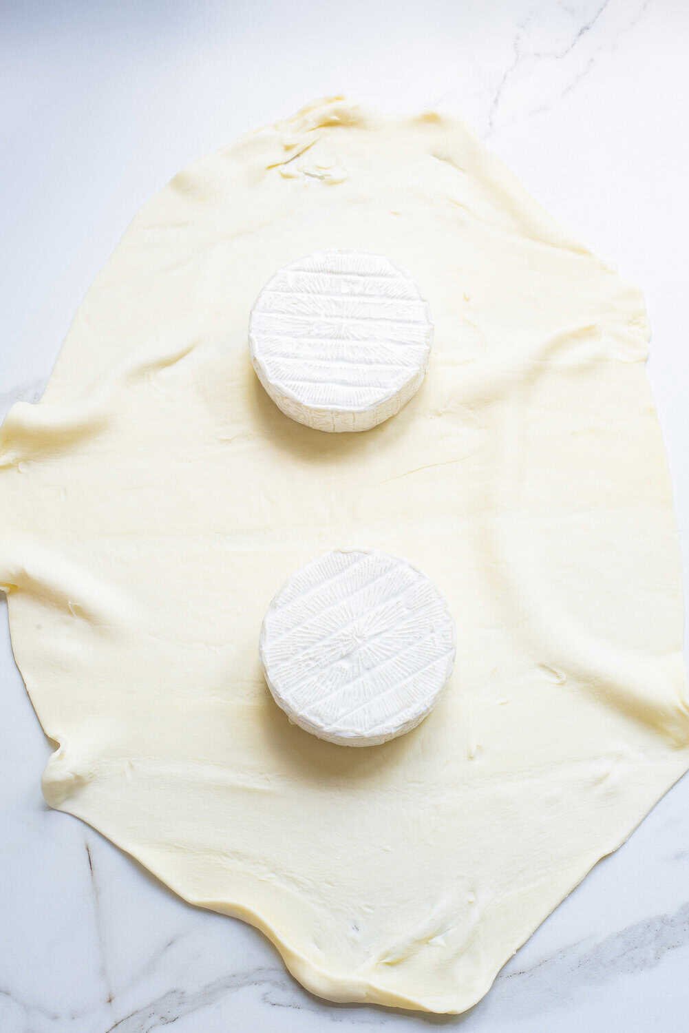 wheels of baked brie on a sheet of puff pastry