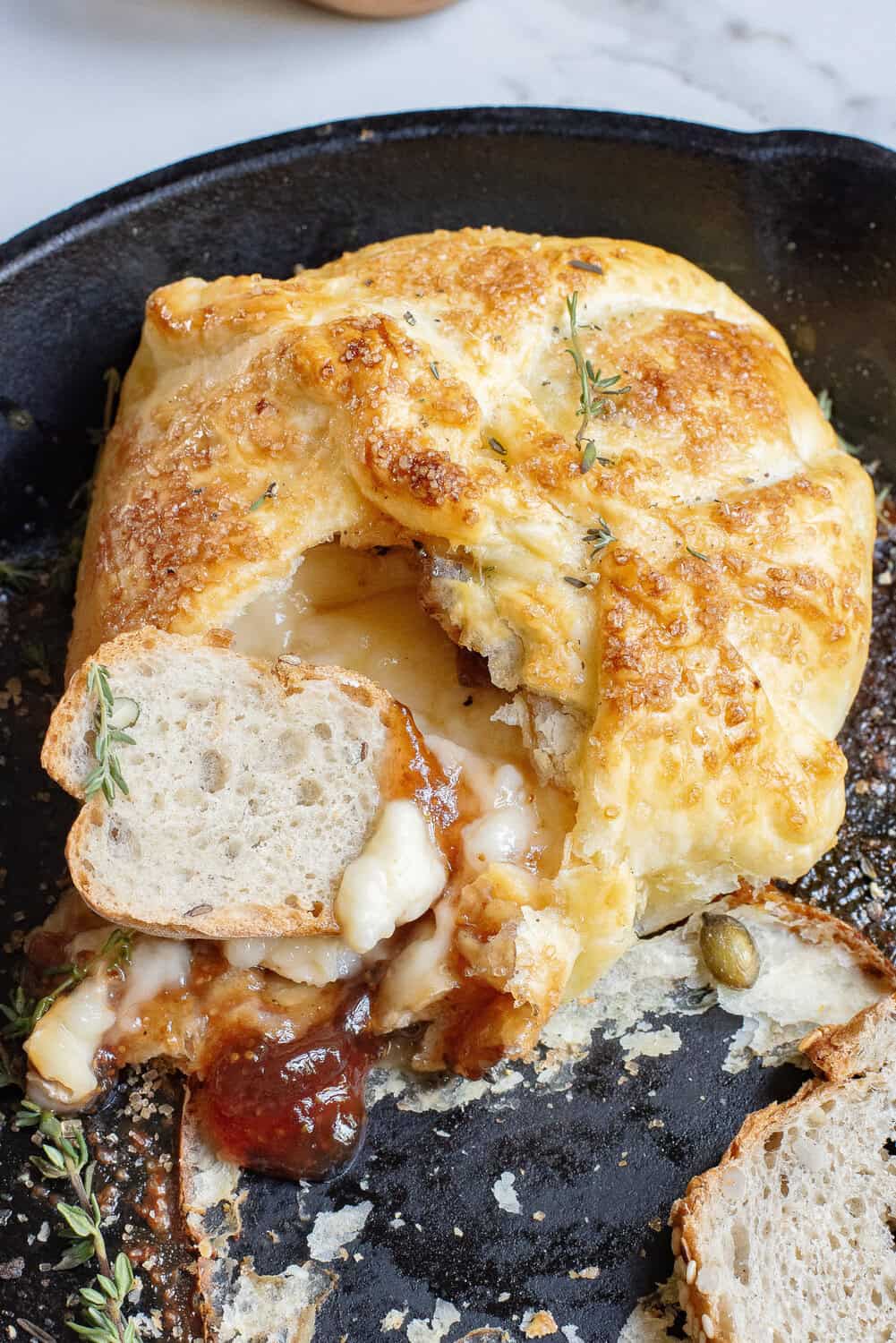 baked brie cut open with a slice of crispy baguette dipping in the cheese and fig jam