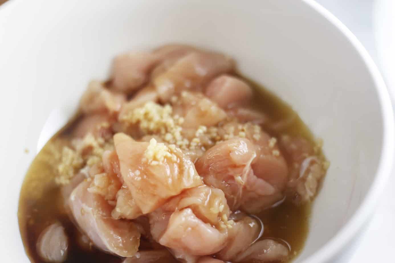 chicken chunks in a white bowl with pineapple juice, garlic and soy sauce