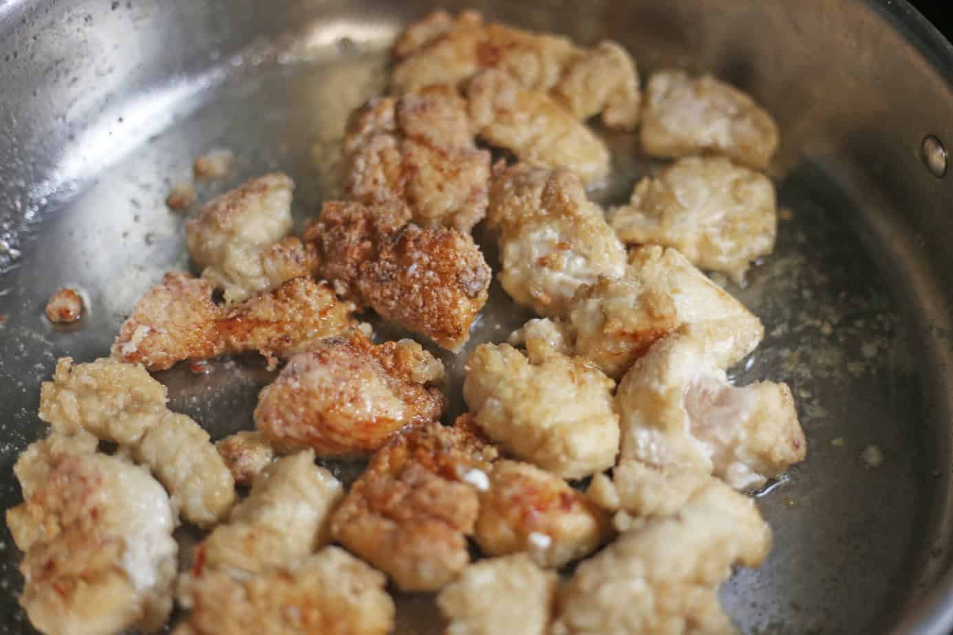 battered chunks of chicken in a skillet partically browned