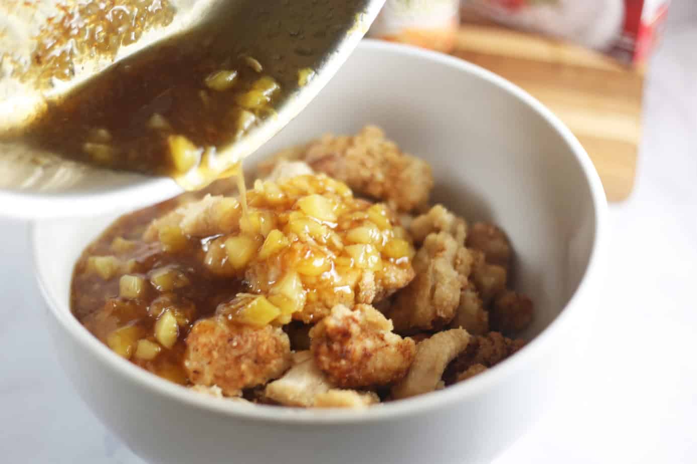 orange pineapple sauce being poured over chicken in a bowl