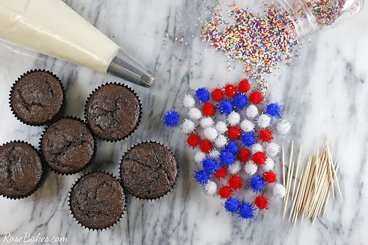 cupcakes, bag of frosting with piping tip, sprinkles, pompoms and toothpicks