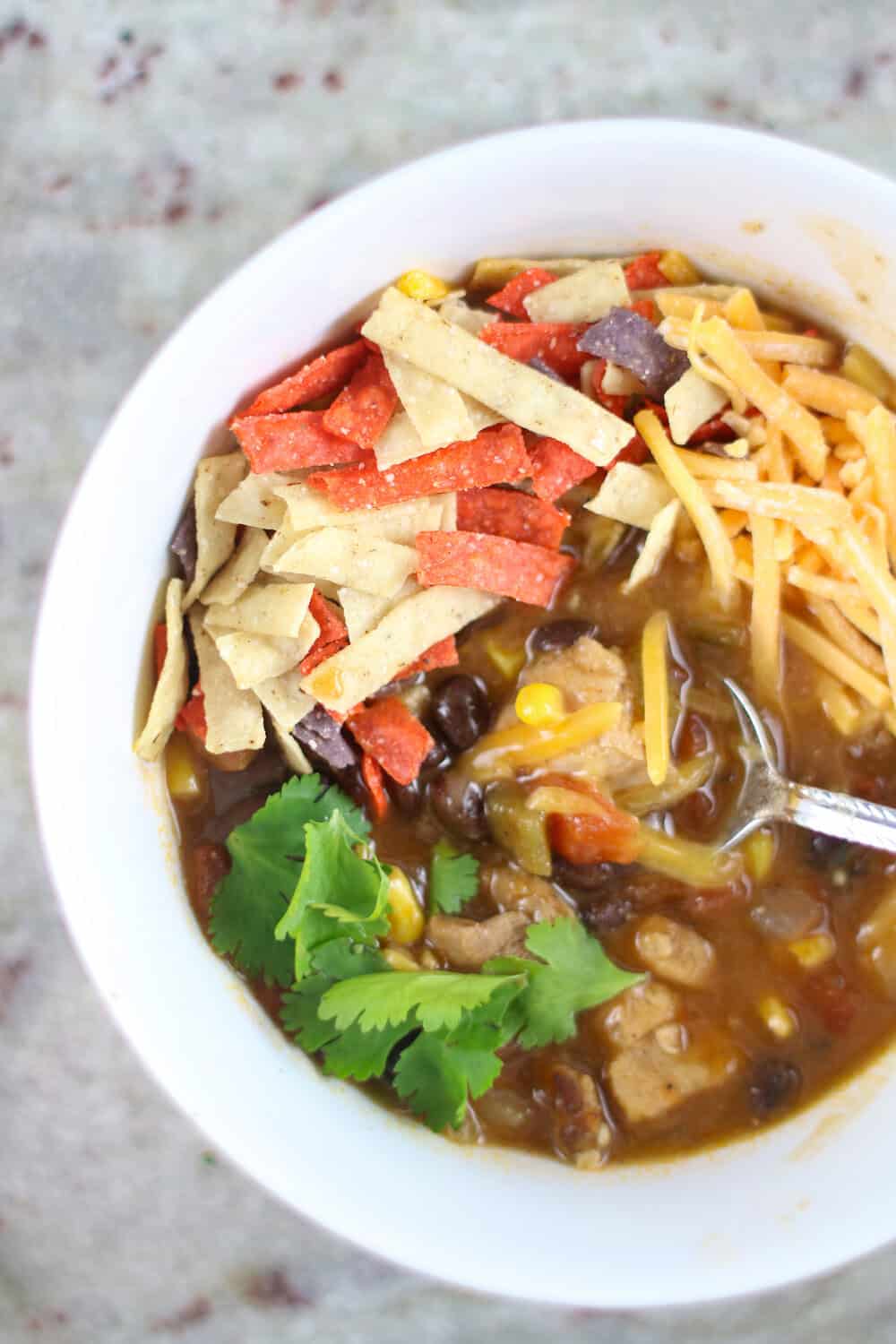 Instant Pot Chicken Tortilla Soup in white bowl with cheese, cilantro and tortilla strips