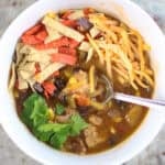 Instant Pot Chicken Tortilla Soup in white bowl with cheese, cilantro and tortilla strips