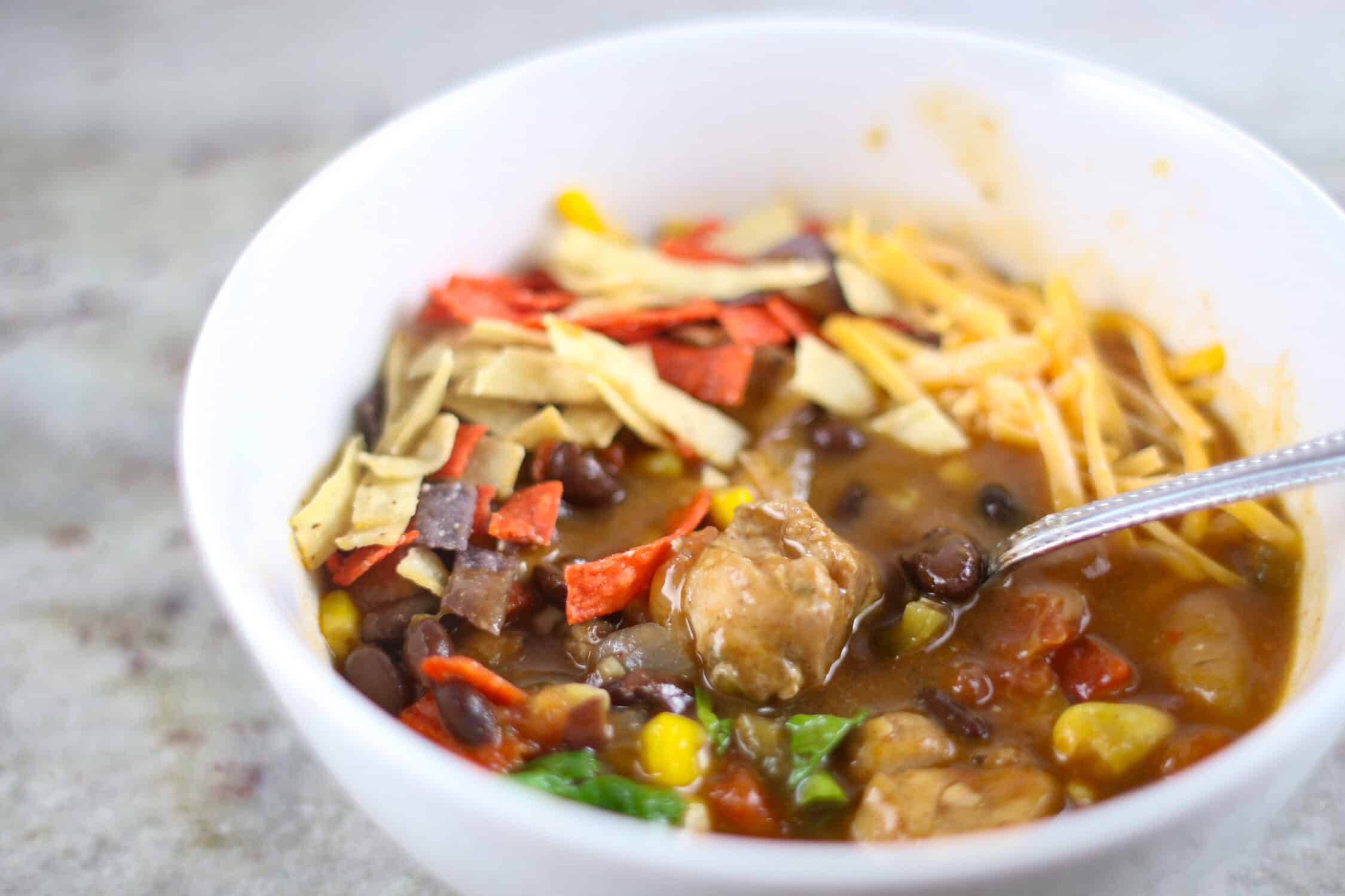 Instant Pot Chicken Tortilla Soup in white bowl with cheese, cilantro and tortilla strips