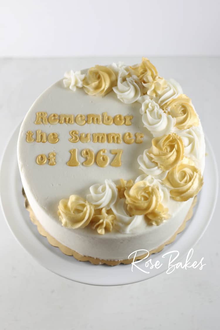 Single tiered buttercream cake with shimmery roses on top and fondant lettering saying Remember the summer of 1967
