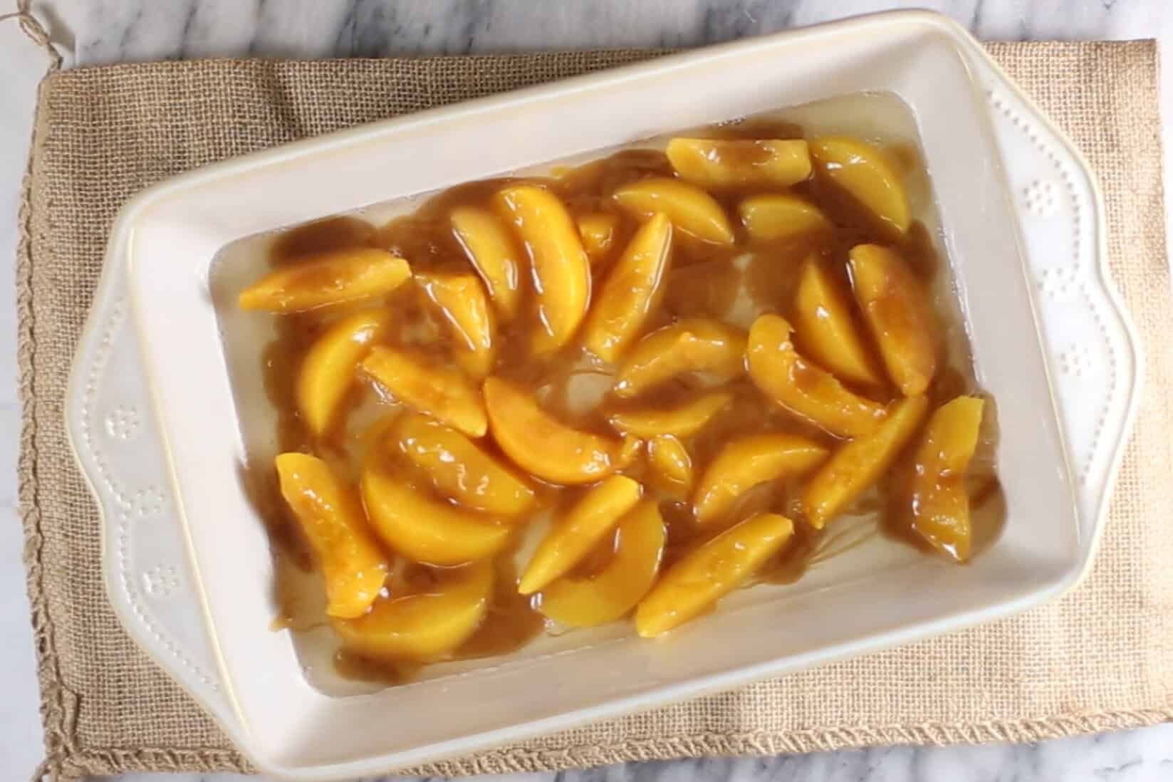 canned peaches poured in a 9x13 baking dish with caramel sauce drizzled over the top