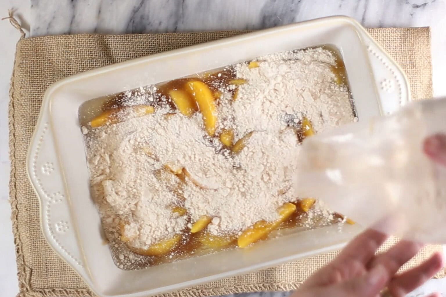 cake mix being poured over peaches and caramel