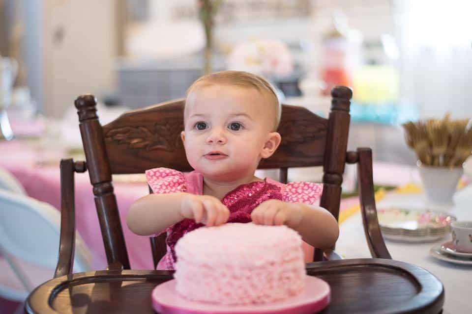 baby girl in high chair grabbing pink smash cake