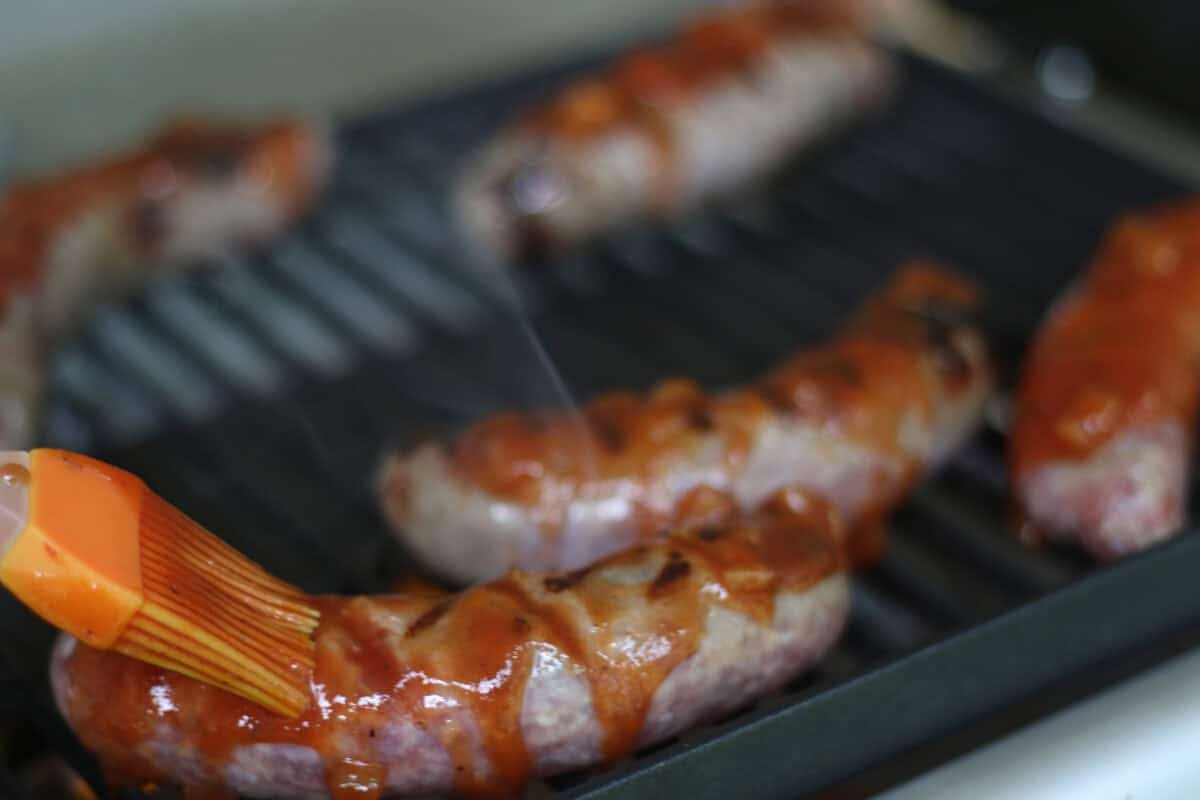 bbq sauce being brushed over brats on a grill