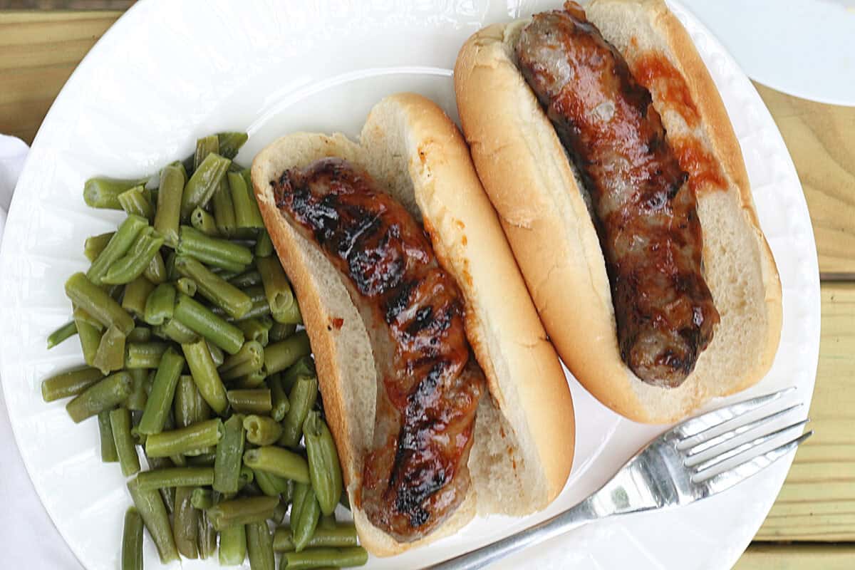 grilled brats on buns on a plate with green beans