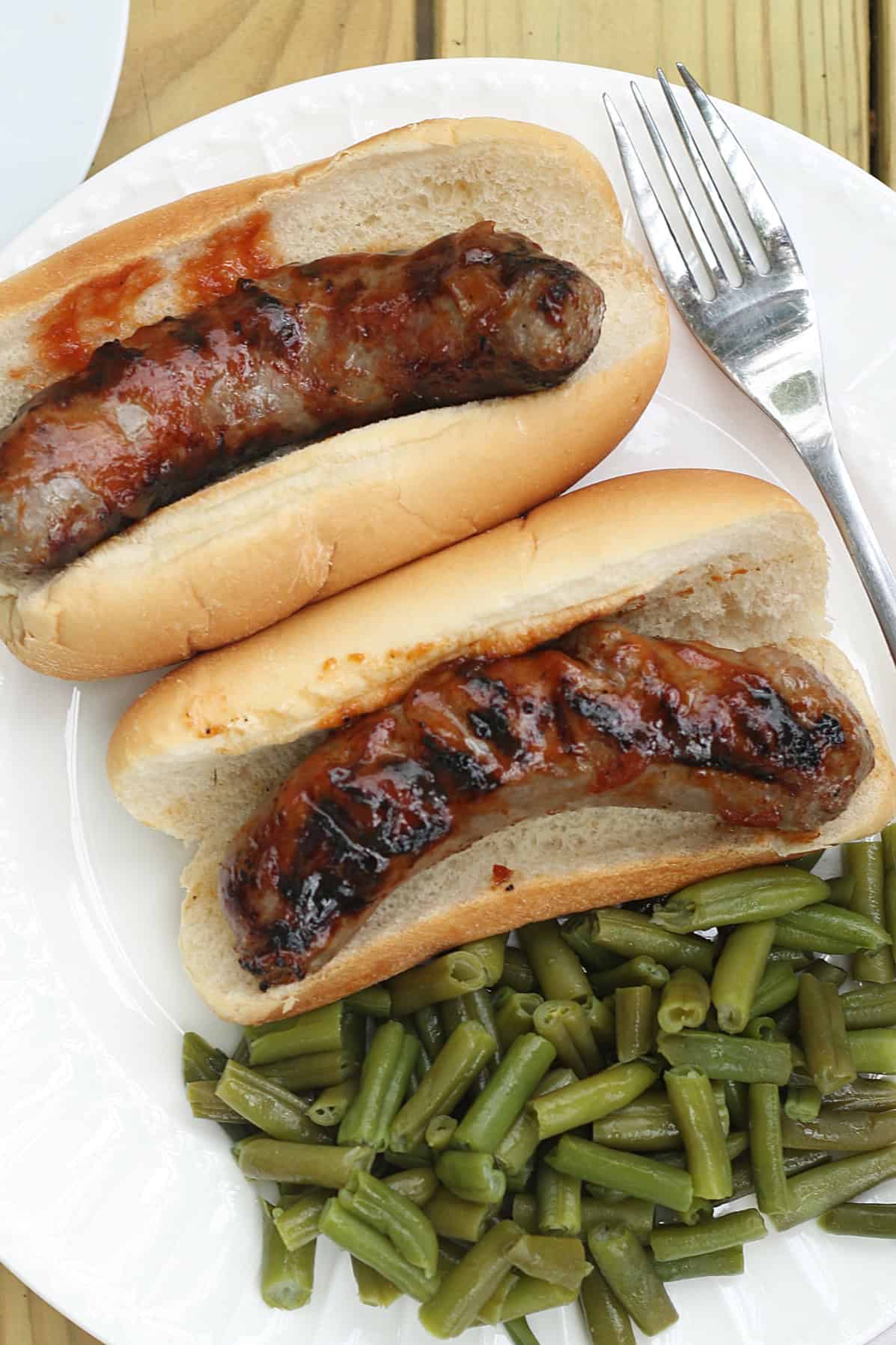 grilled bratwurst on buns on a plate with green beans
