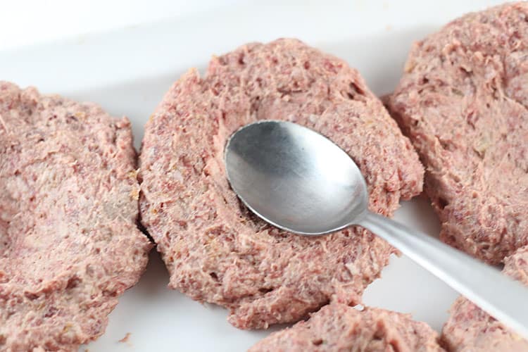 using spoon to make dent in burger so it cooks evenly