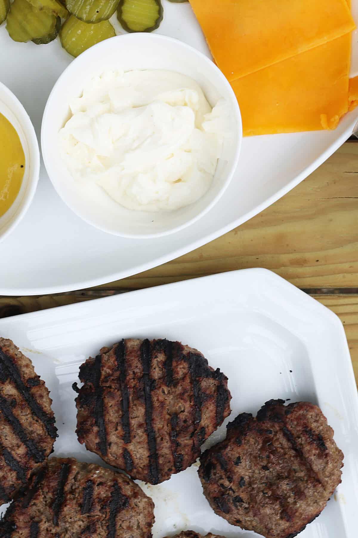 grilled burgers on a platter with another platter of toppings