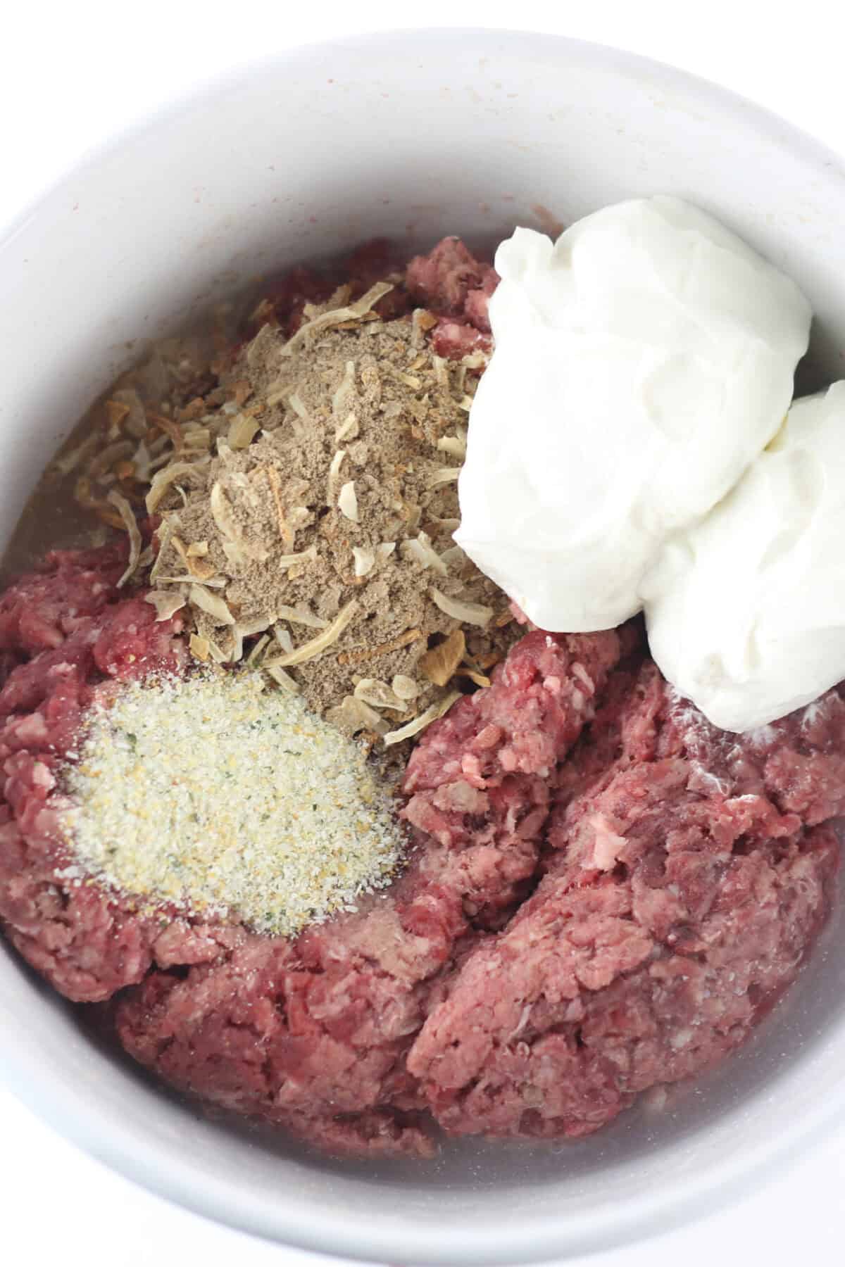 raw hamburger meat with seasonings and sour cream in a bowl