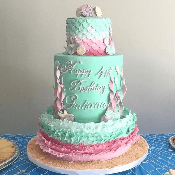 Mermaid Birthday Cake with seashell topper. Bottom tier is pink, mint, and white ruffles, mint double barrel middle tier with seaweed up the sides, and the top tier is covered with mermaid scales in mint, white, and pink.