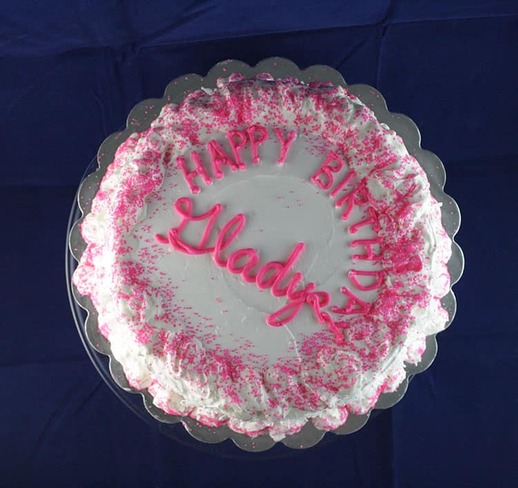 White single tiered cake with piped wording saying happy birthday Gladyse