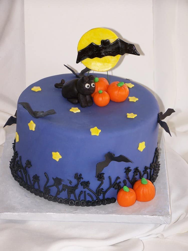 purple cake with black bats, orange pumpkins and a black fondant cat on top perfect for halloween