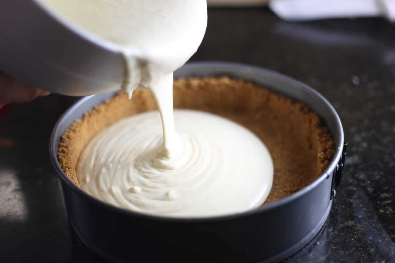 pouring eggnog cheesecake filling into gingersnap crust