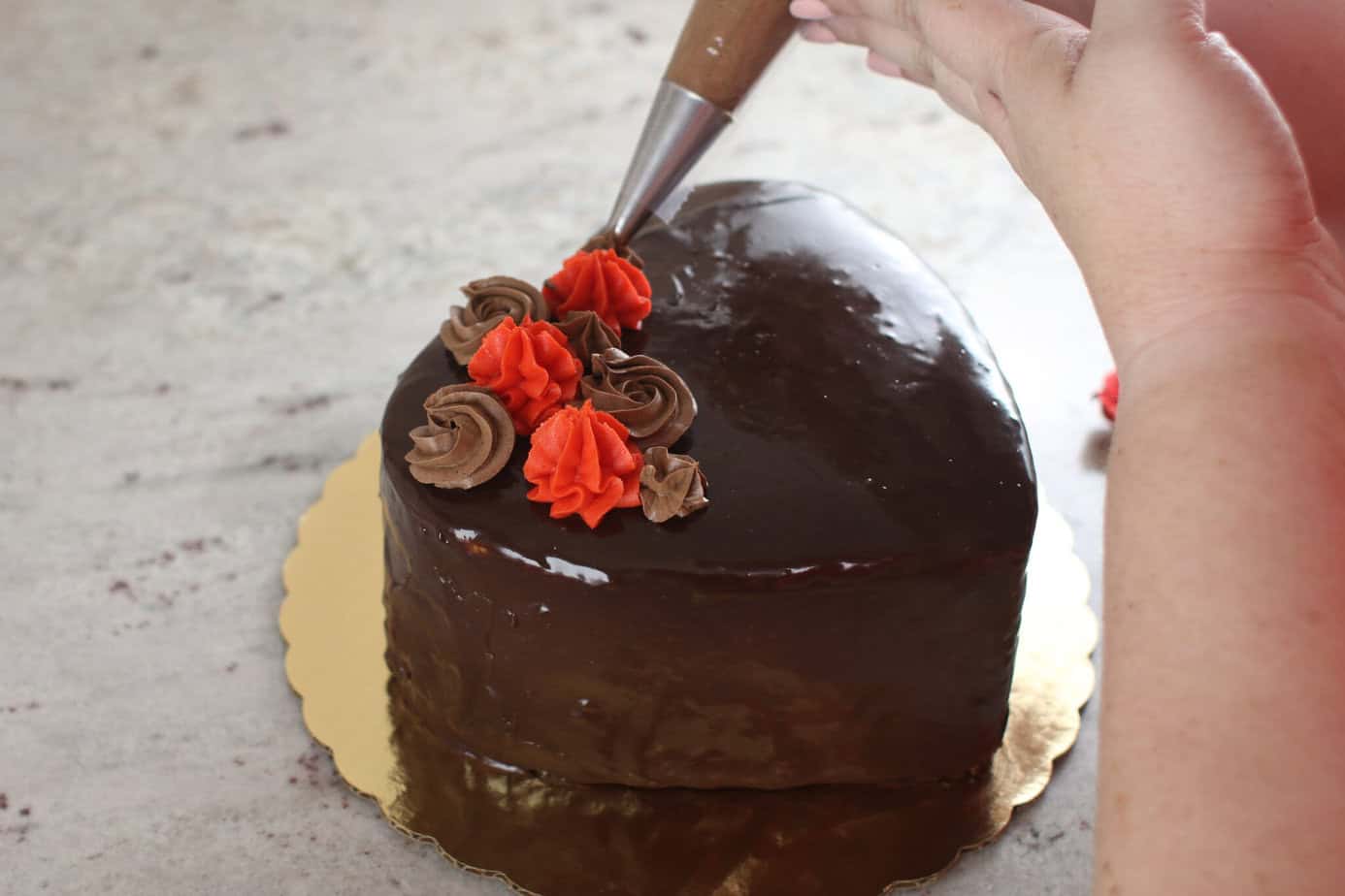 piping brown decorations onto ganache covered heart shaped cake
