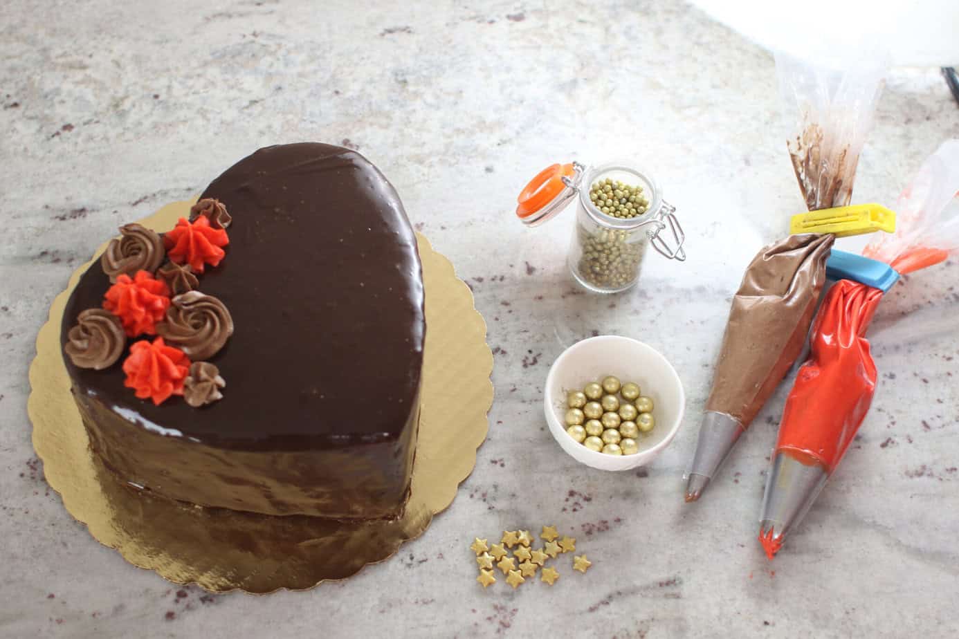 heart cake with bags of frosting and gold sprinkles next to it