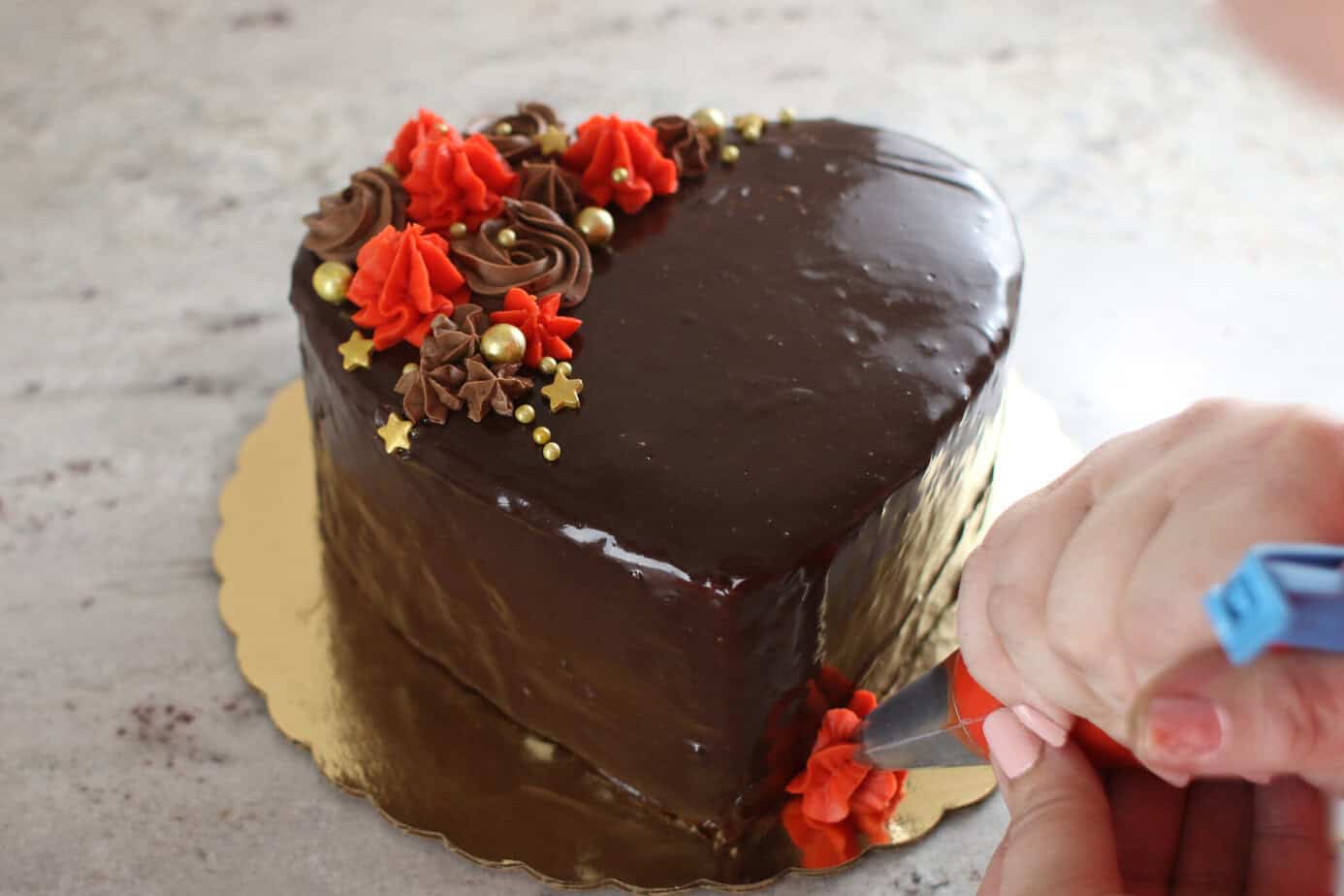 piping red frosting onto the border of a heart cake