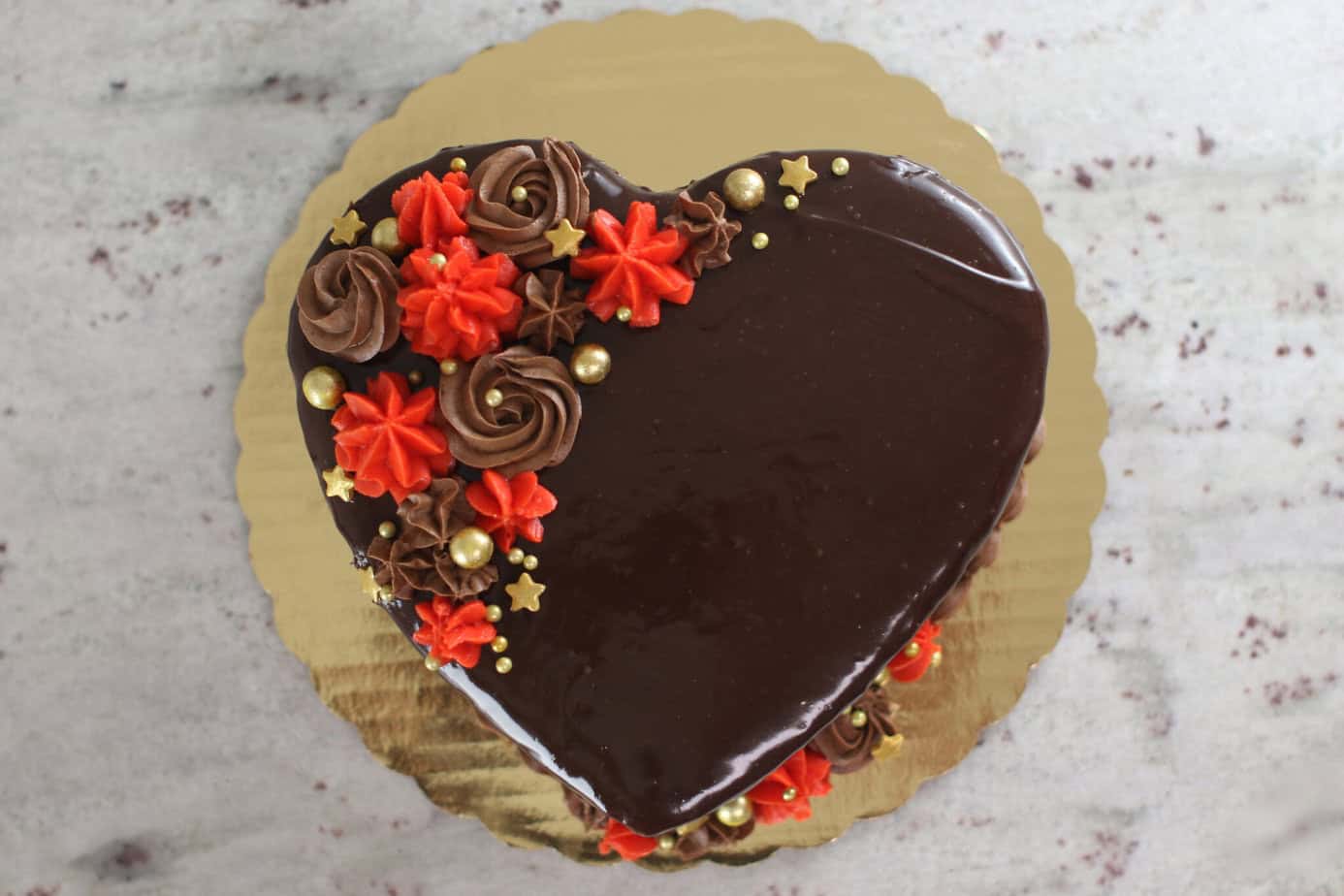 heart cake covered in ganache and deorated with red and brown frosting and gold sprinkles