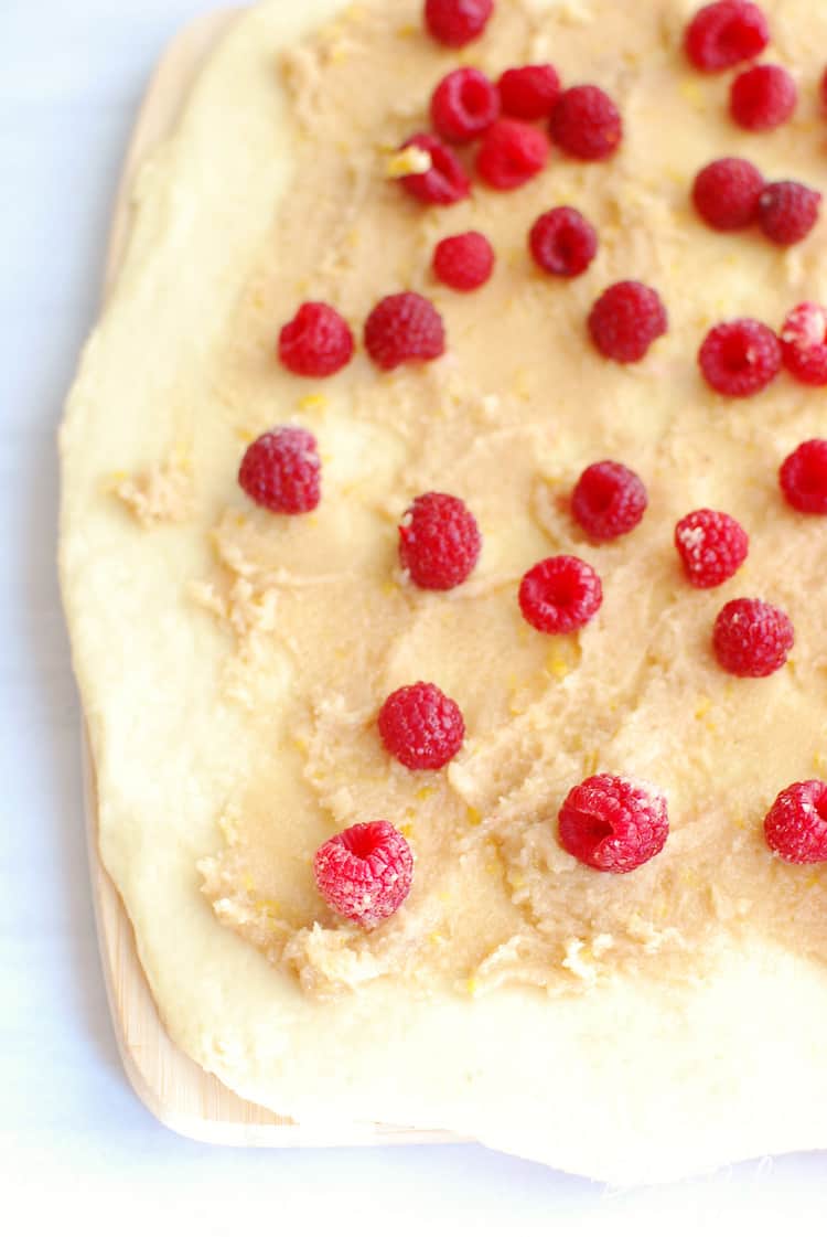 Raspberry Cinnamon Rolls dough rolled out on cutting board with filling and raspberries on top