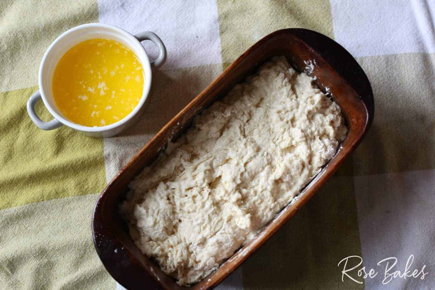 dough in baking loaf pan with melted butter in cup on side