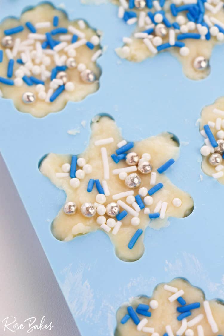 close up of silicone snowflake molds filled with white chocolate fudge and sprinkles