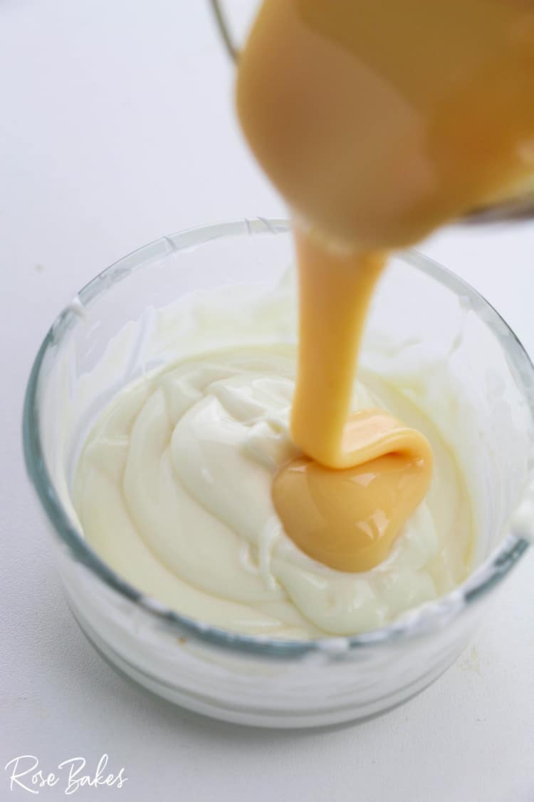 Sweetened condensed milk being poured into the bowl of melted white chocolate