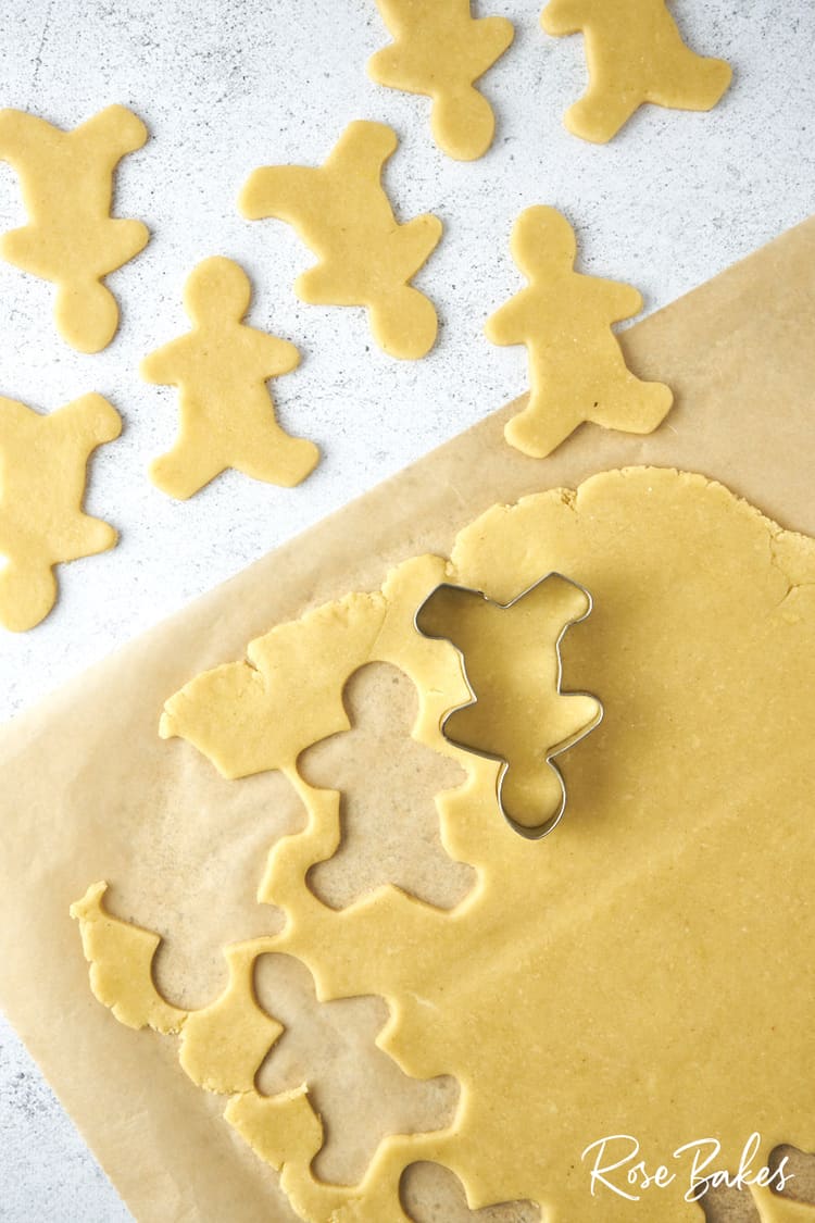 Sheet of cookie dough with shapes cut out with the gingerbread man cookie cutter. It is turned upside down to make the reindeer shape.