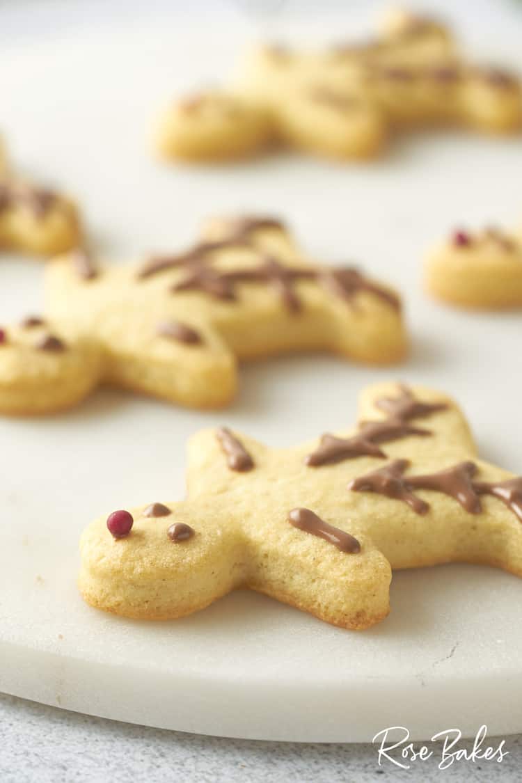 close up of the finished Christmas reindeer cookie. The eyes, ears, and antlers are piped chocolate and the nose is a red sugar pearl.