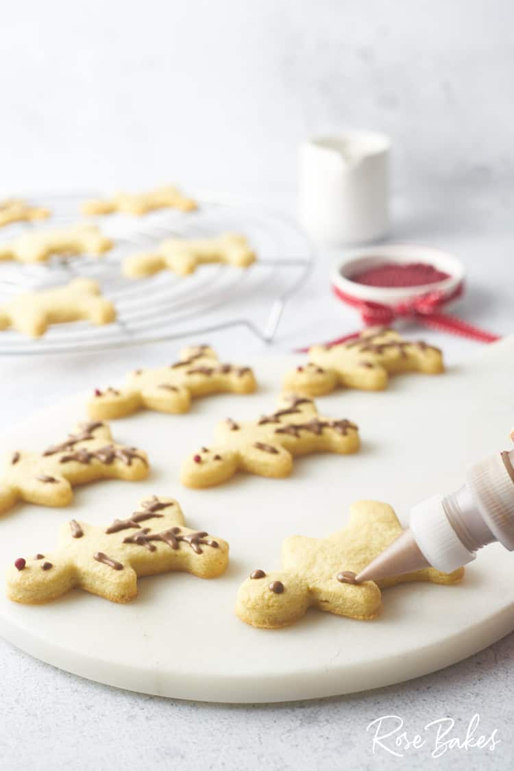 The cookies being decorated with melted chocolate on a white platter.