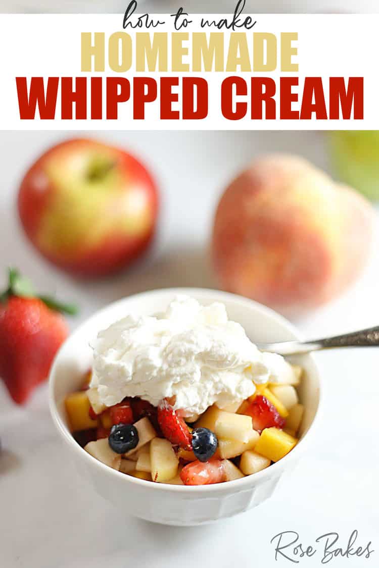 White bowl filled with fruit salad and topped with homemade whipped cream. Whole fresh fruit is in the background.