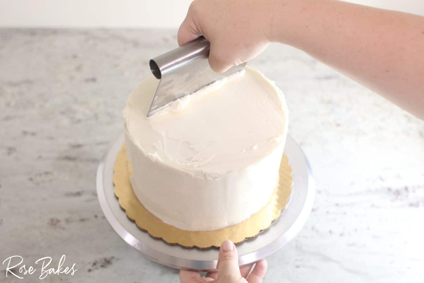 benchcraper smoothing top of buttercream icing cake 