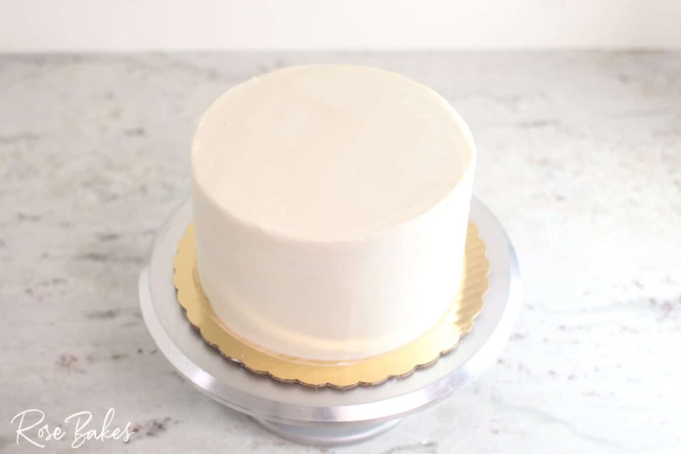 bottom tier of buttercream icing cake smoothed and on cake stand sharp edge