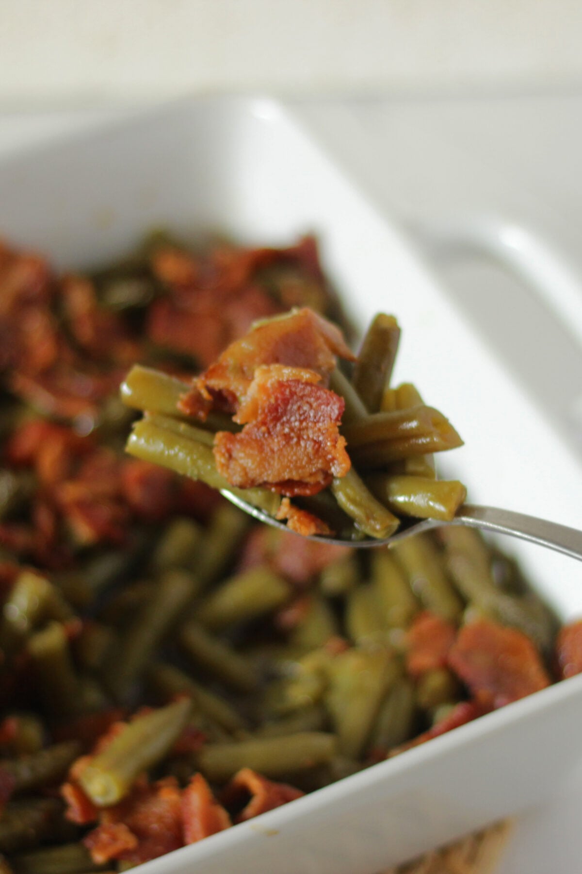 a spoon of green beans with bacon, brown sugar and soy sauce