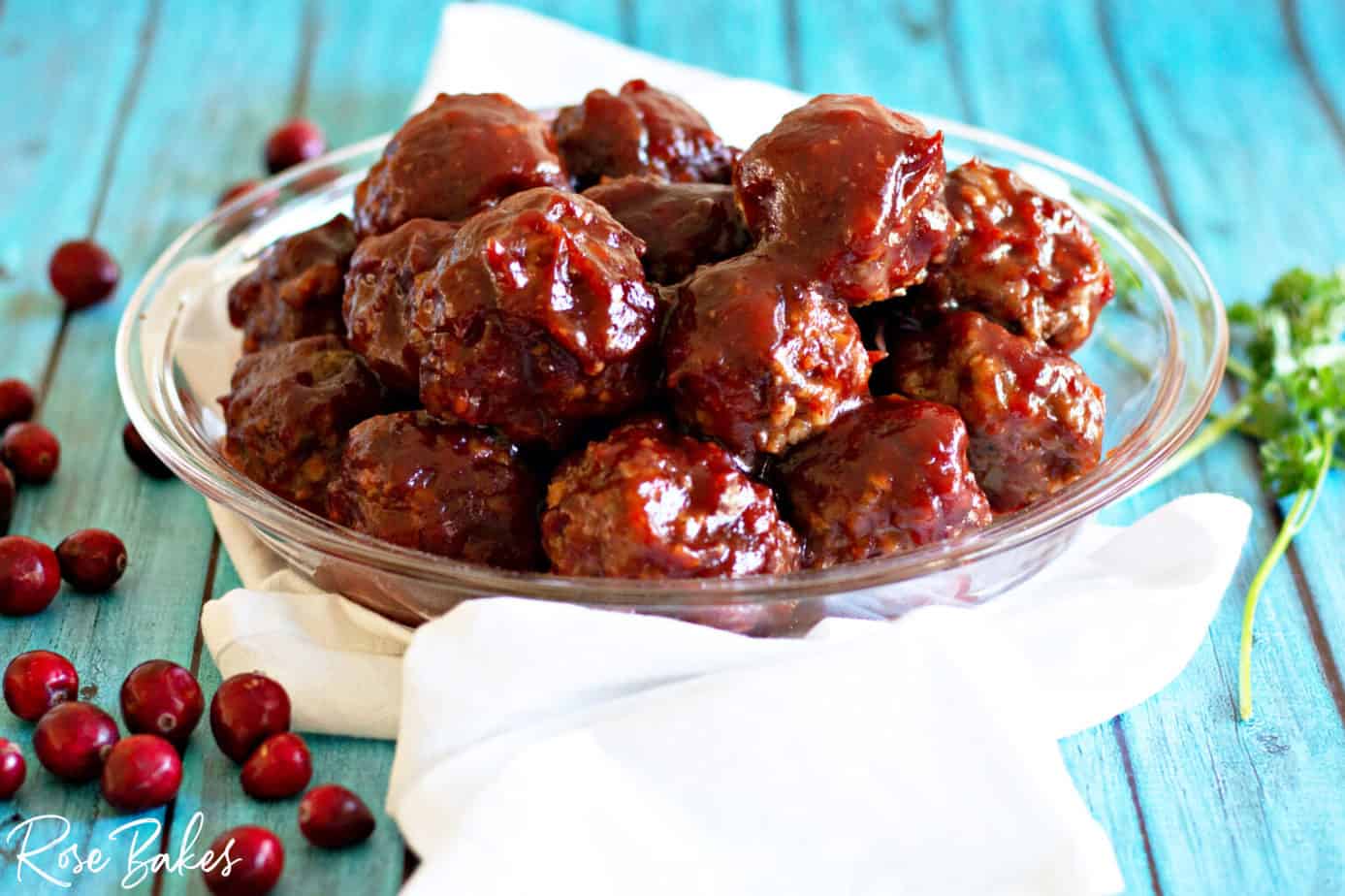 Bowl of Cranberry BBQ Meatballs on a blue backgrounds and fresh cranberries next to the bowl.