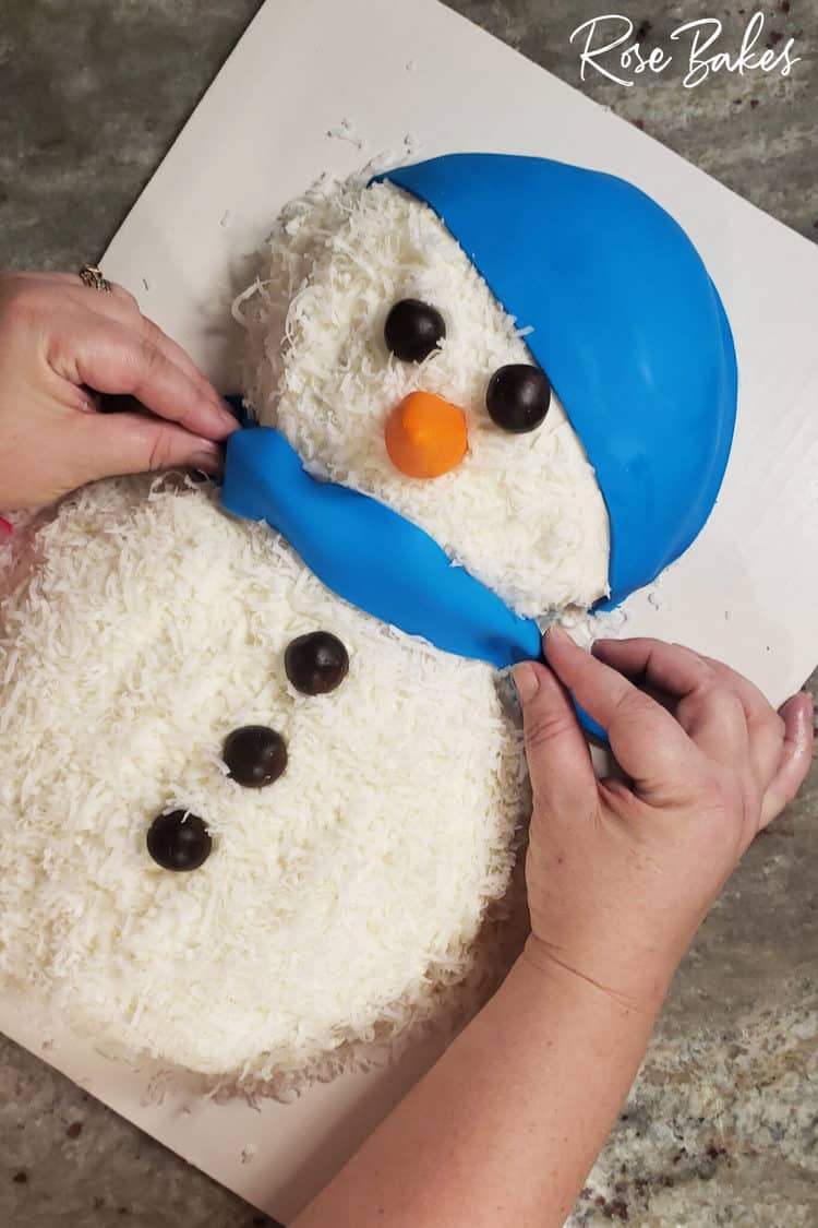 blue fondant scarf being placed on gluten-free coconut cake