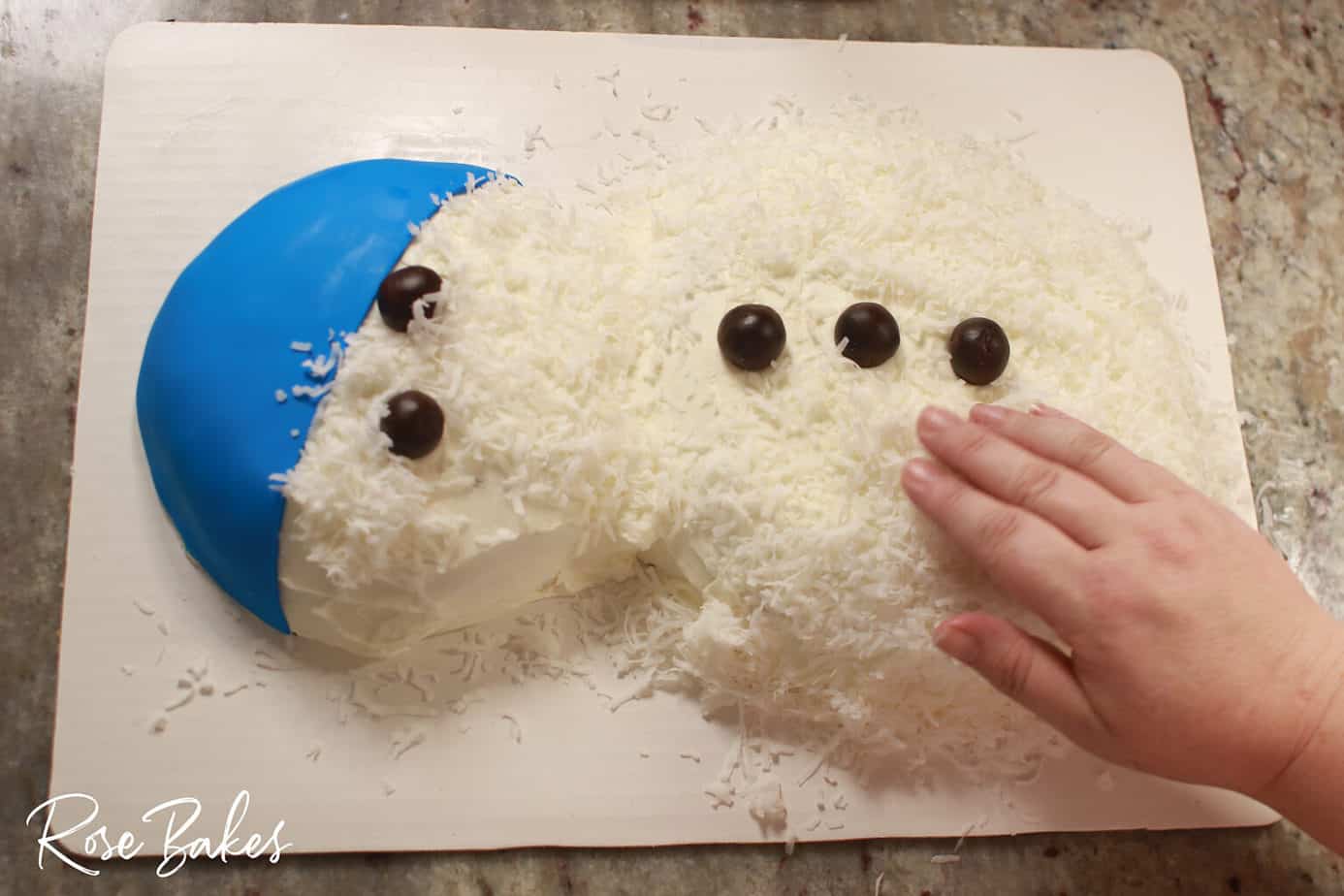 coconut being pressed into the buttercream icing on honey coconut cake for snowman effect
