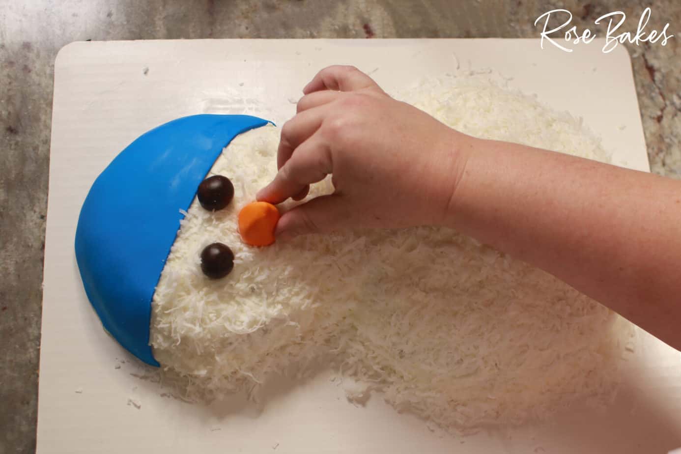 orange fondant nose being placed on honey coconut cake