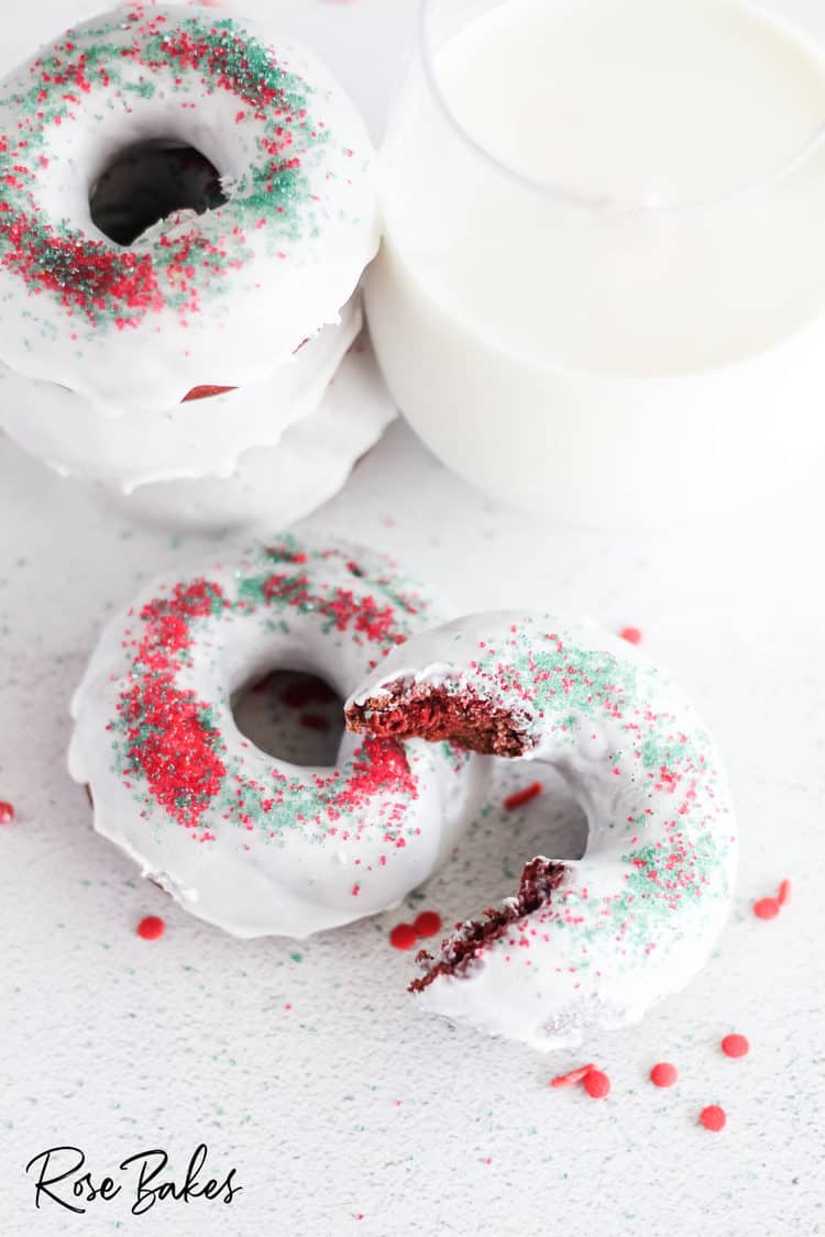 Stack of donuts next to glass of milk. Two donuts in front with one of the eaten to show the red inside.