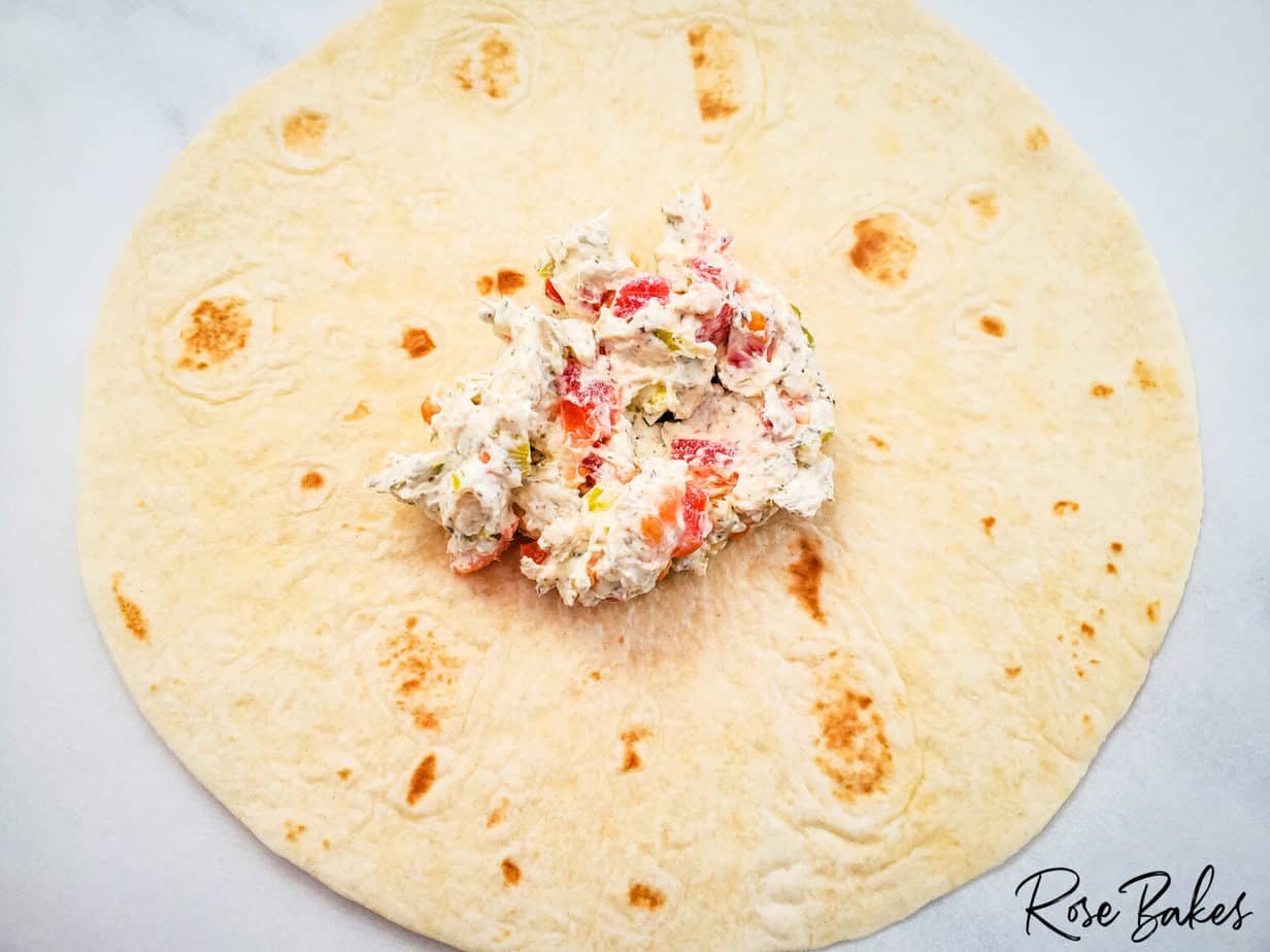 adding cream cheese spread to a large tortilla
