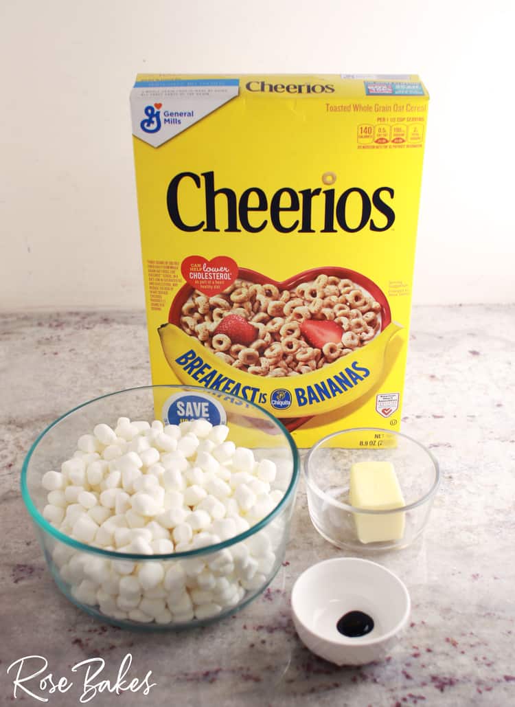 Box of Cheerios, bowl of mini marshmallows, butter in bowl and green food coloring in bowl all sitting on counter