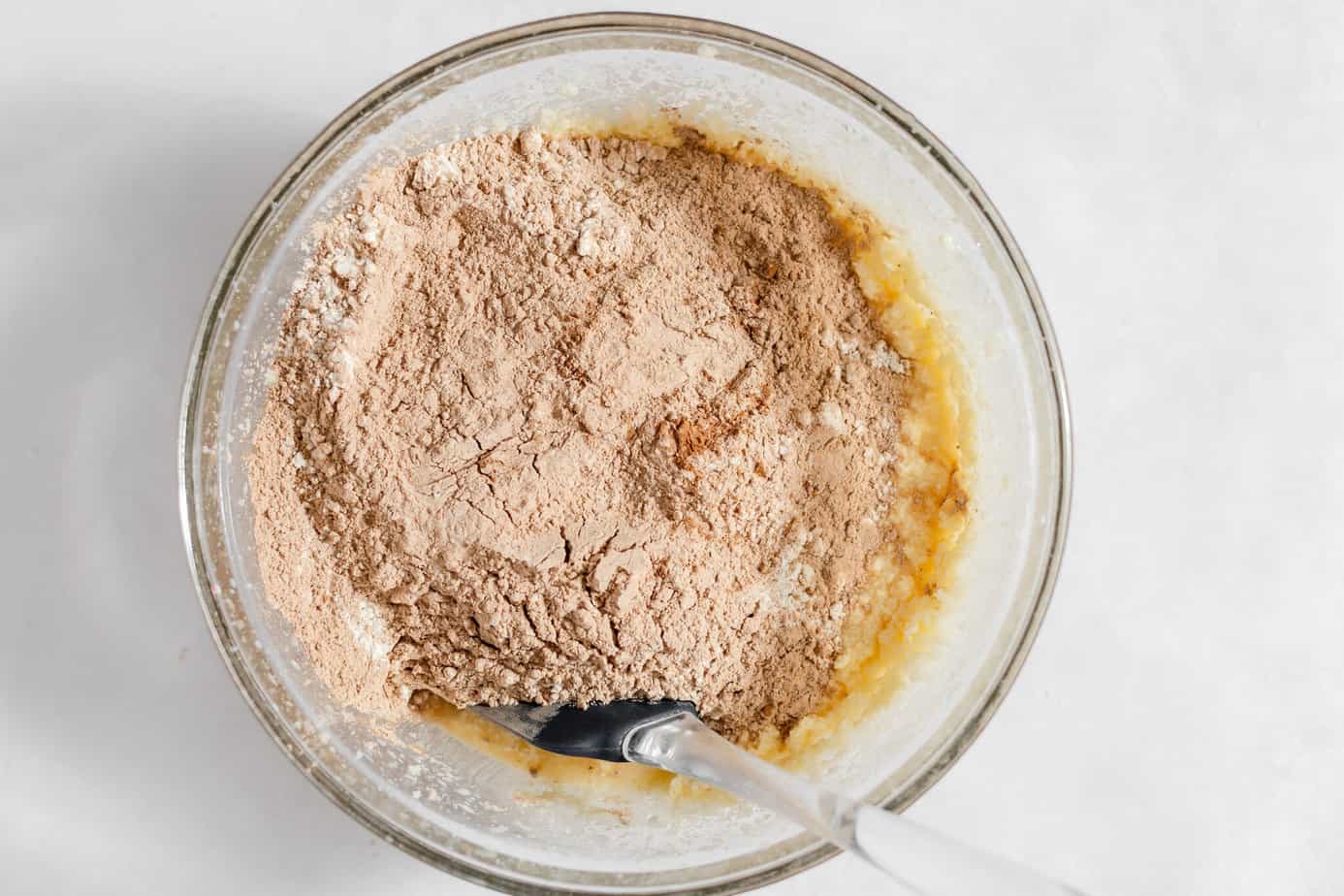 Dry ingredients added to the wet ingredients in a glass mixing bowl.