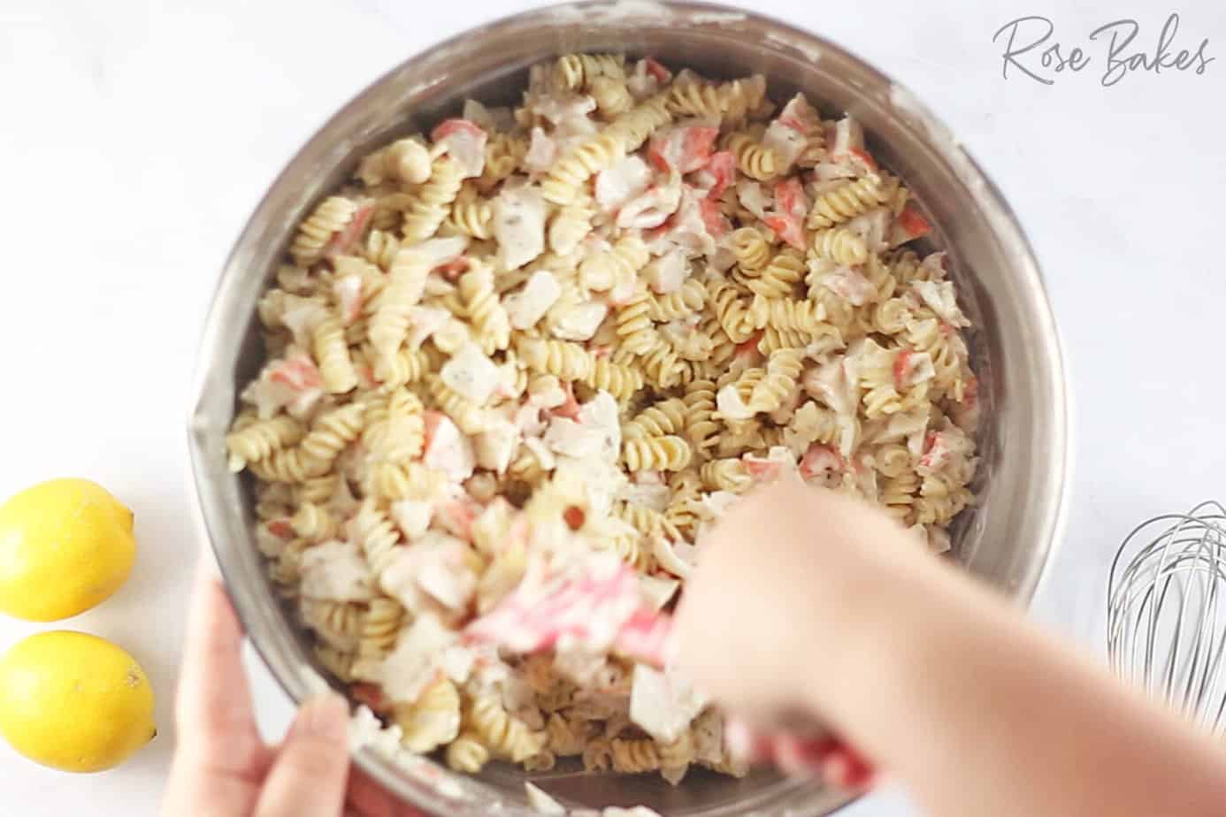 mixing creamy crab salad mixture with cooked pasta in a silver bowl